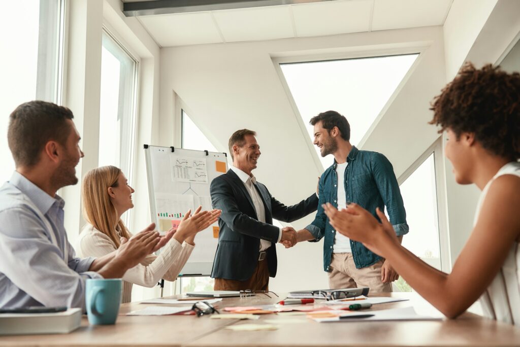 Welcome to our team Two cheerful colleagues shaking hands and smiling while having a meeting in the